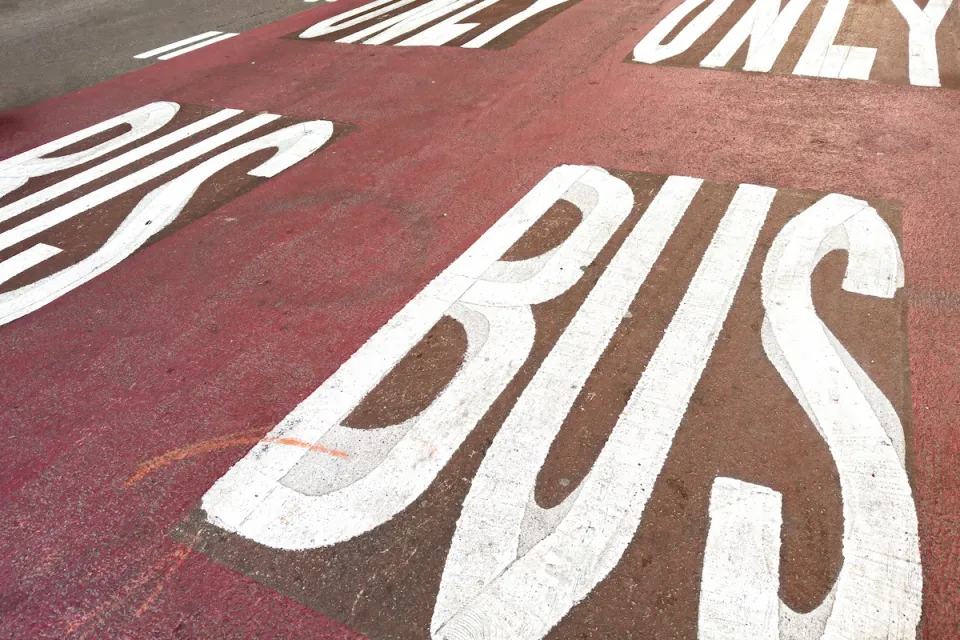 White BUS ONLY letters on red painted bus lane on street.